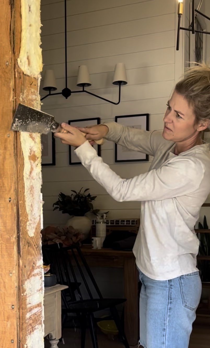 A person using a pull saw scrape insulation from a house frame rough opening 