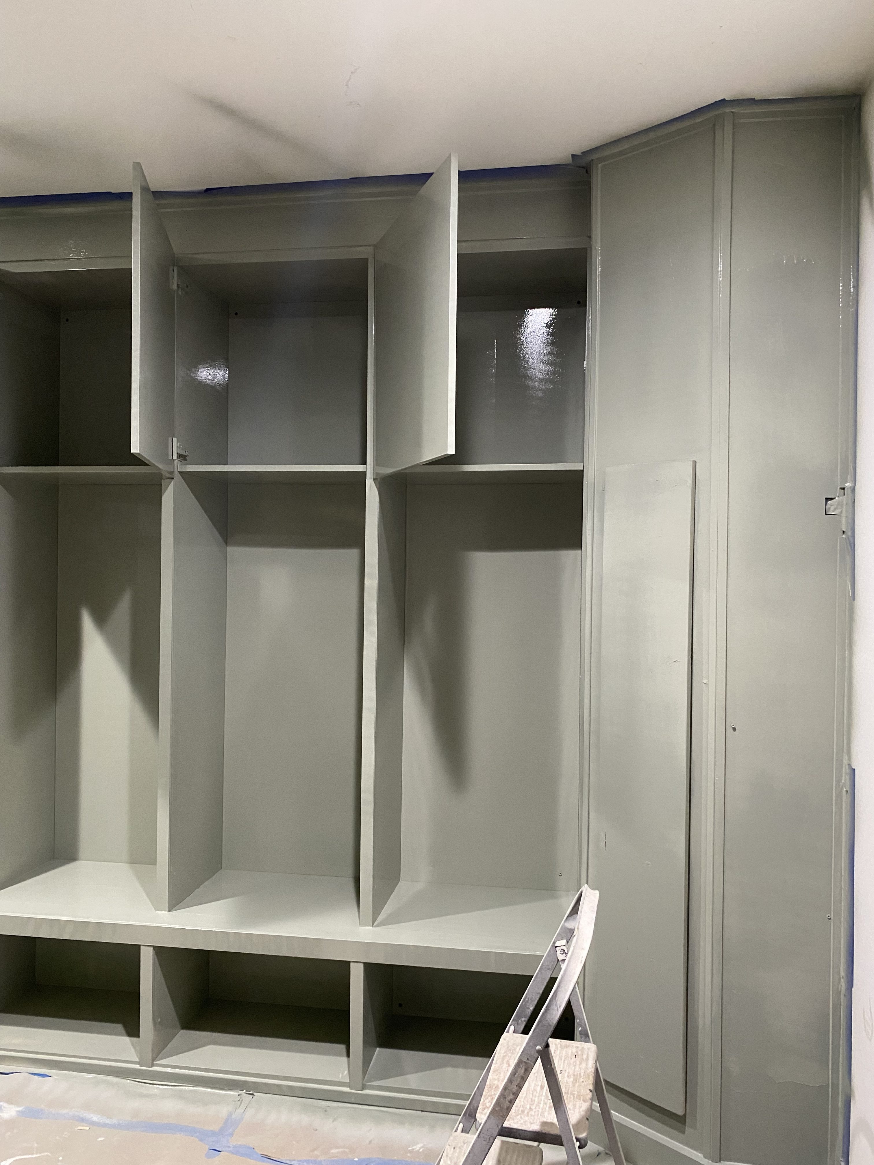 A partially finished built-in cabinet with several open and closed shelves, painted in a light green color, next to a ladder.